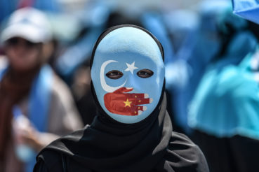 TOPSHOT - A demonstrator wearing a mask painted with the colours of the flag of East Turkestan and a hand bearing the colours of the Chinese flag attends a protest of supporters of the mostly Muslim Uighur minority and Turkish nationalists to denounce China's treatment of ethnic Uighur Muslims during a deadly riot in July 2009 in Urumqi, in front of the Chinese consulate in Istanbul, on July 5, 2018. - Nearly 200 people died during a series of violent riots that broke out on July 5, 2009 over several days in Urumqi, the capital city of the Xinjiang Uyghur Autonomous Region, in northwestern China, between Uyghurs and Han people. (Photo by OZAN KOSE / AFP)        (Photo credit should read OZAN KOSE/AFP/Getty Images)