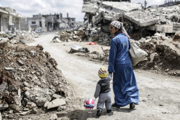 A Kurdish Syrian woman walks with her child past the ruins of the town of Kobane, also known as Ain al-Arab, on March 25, 2015. Islamic State (IS) fighters were driven out of Kobane on January 26 by Kurdish and allied forces. AFP PHOTO/YASIN AKGUL        (Photo credit should read YASIN AKGUL/AFP/Getty Images)